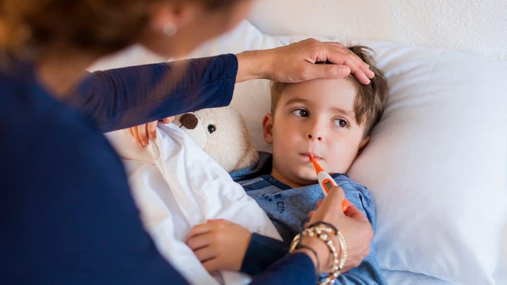 Mulher com mão na testa de menino doente enquanto segura termômetro na boca dele