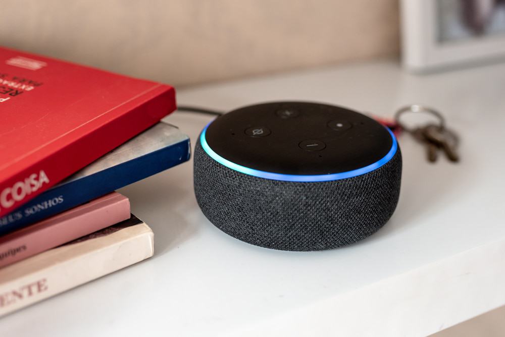 Imagem mostra o dispositivo da Amazon, o Echo Dot, que funciona com a assistente virtual Alexa, em cima de uma mesa; ao lado, livros empilhados