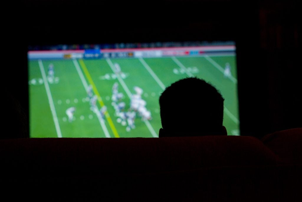 silhueta de um homem assistindo um jogo de futebol americano na tv