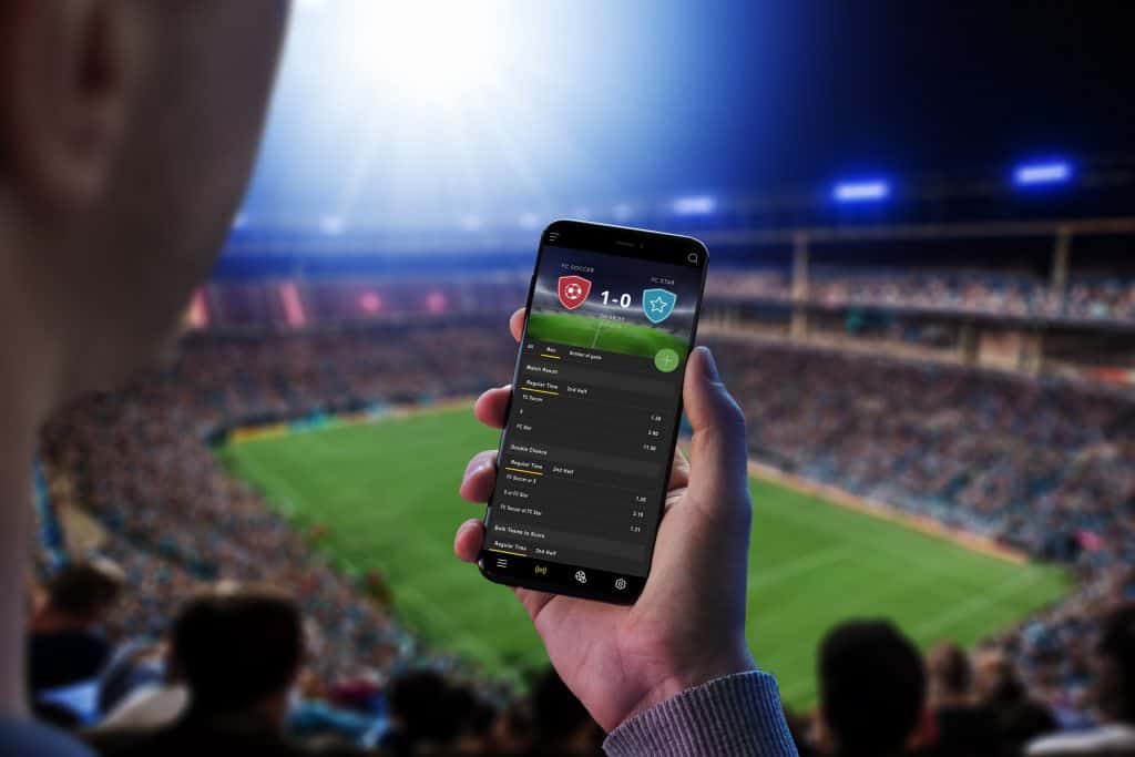 Pessoa em um estádio segurando um smartphone com uma bet na tela