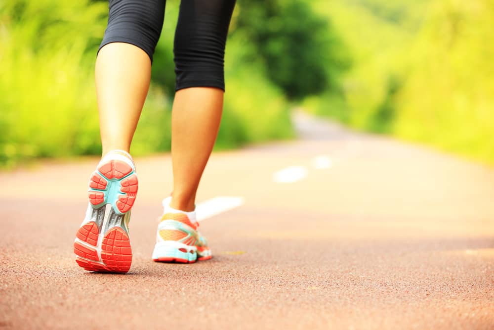 Imagem mostra um par de pernas femininas com tênis e roupa fitness, caminhando por uma rua