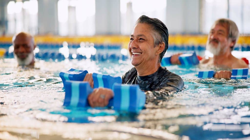 Halteres, grupo e mulher madura em piscina para exercícios, corpo saudável e músculos fortes. Terapia aquática, água e aula de aeróbica para fitness, fisioterapia ou reabilitação de pessoas idosas.